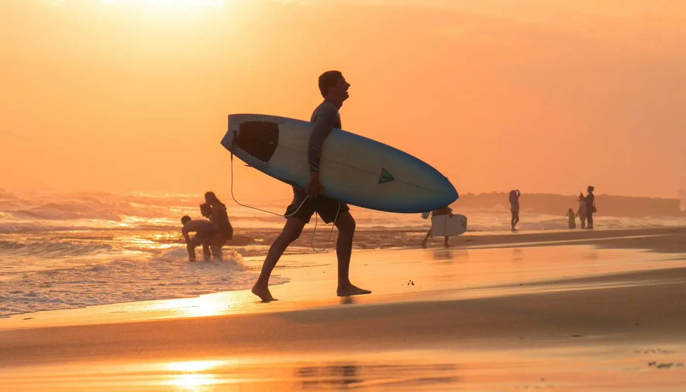 Surfer walking along a Bali beach at sunset